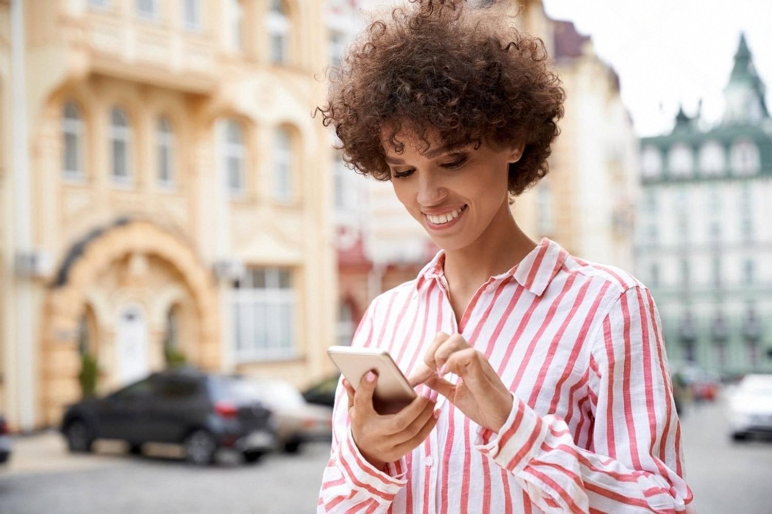 Smiling guest completing a mobile hotel check-in on her smartphone in the street